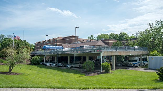 A hospital building with a parking area beneath and surrounding greenery.