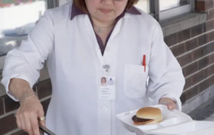 A person in a white uniform serving a sandwich.