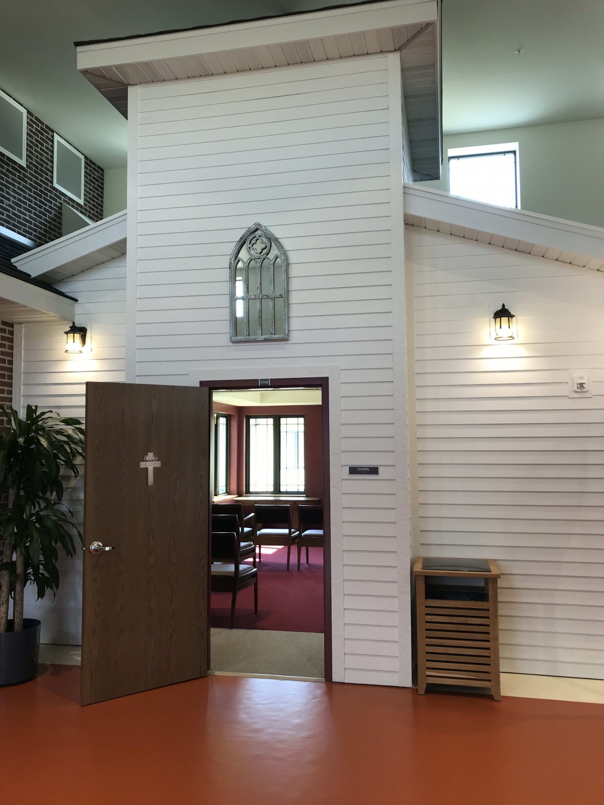 Interior view of a chapel room with an open door and decorative window.