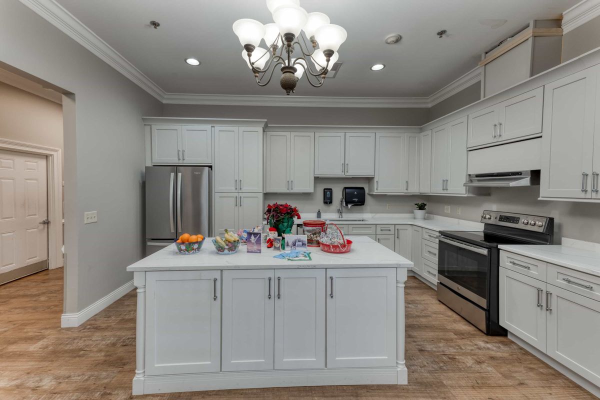 A modern kitchen with white cabinets and a central island, featuring stainless steel appliances and a decorative chandelier.