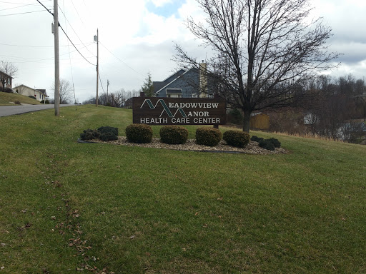 A welcoming sign located on a grassy hill, surrounded by landscaping and under a cloudy sky.