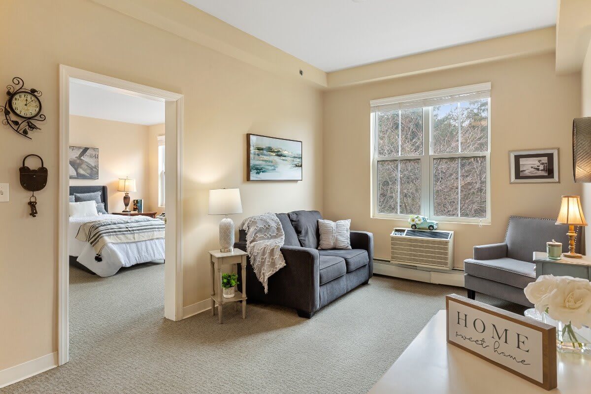A cozy and bright apartment interior featuring a living room with a sofa and a view into the bedroom.