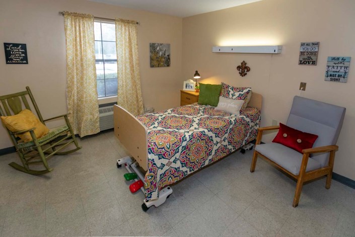 A cozy bedroom with a neatly made single bed, an armchair, and a well-lit window.
