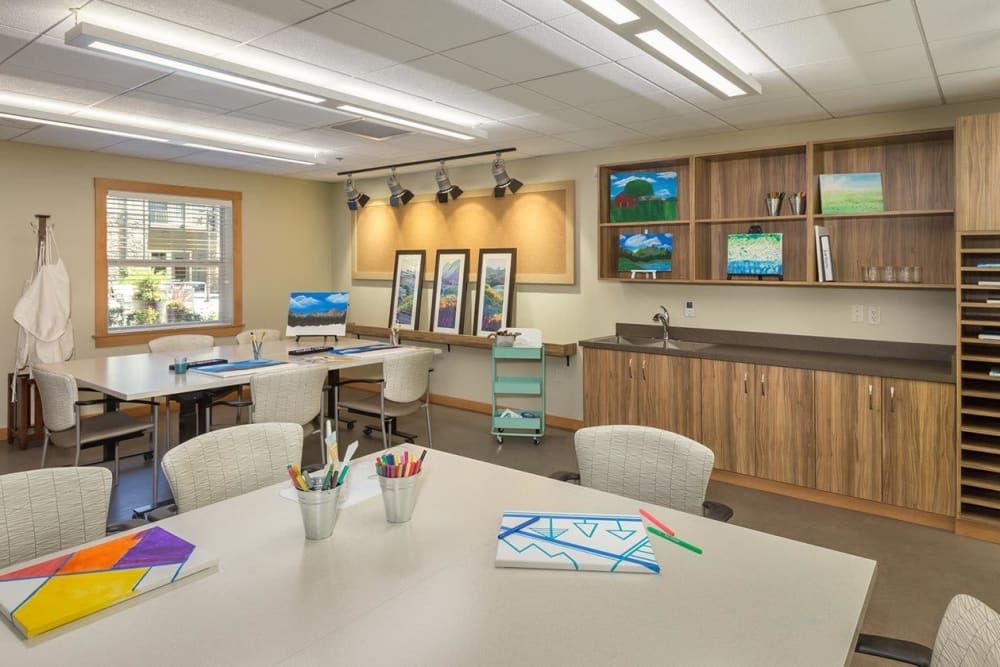 A well-equipped art studio with tables, art supplies, and paintings displayed on the walls.