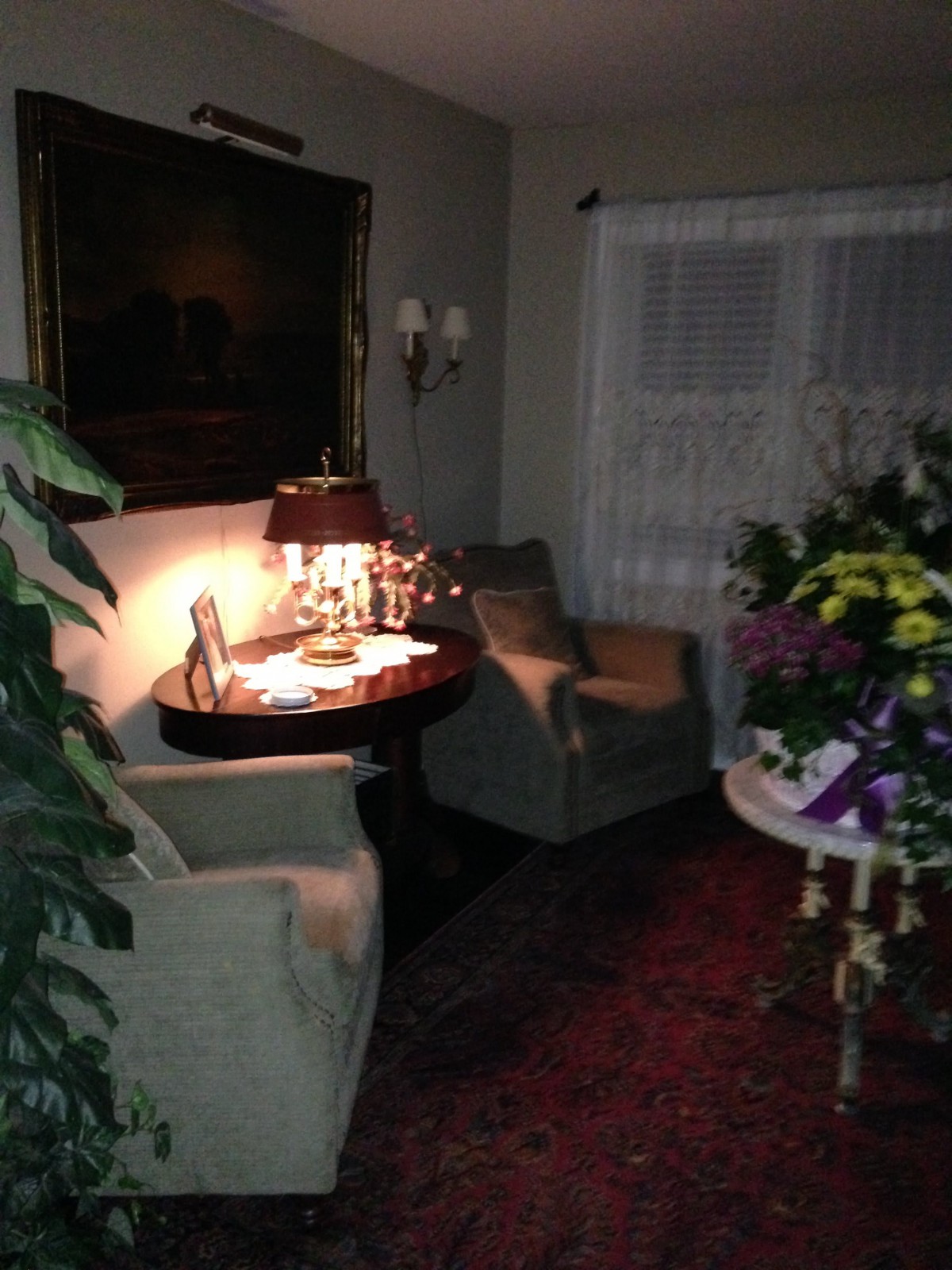 A cozy living room featuring comfortable armchairs, a round table with a lamp, and vibrant floral arrangements.