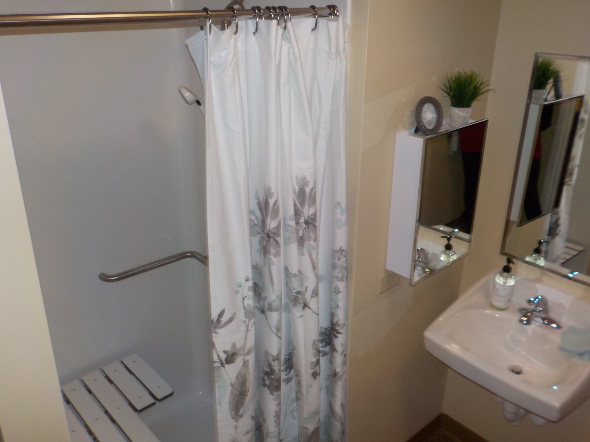 A bathroom featuring a shower with a floral curtain, a sink with a mirror above, and a small plant for decoration.