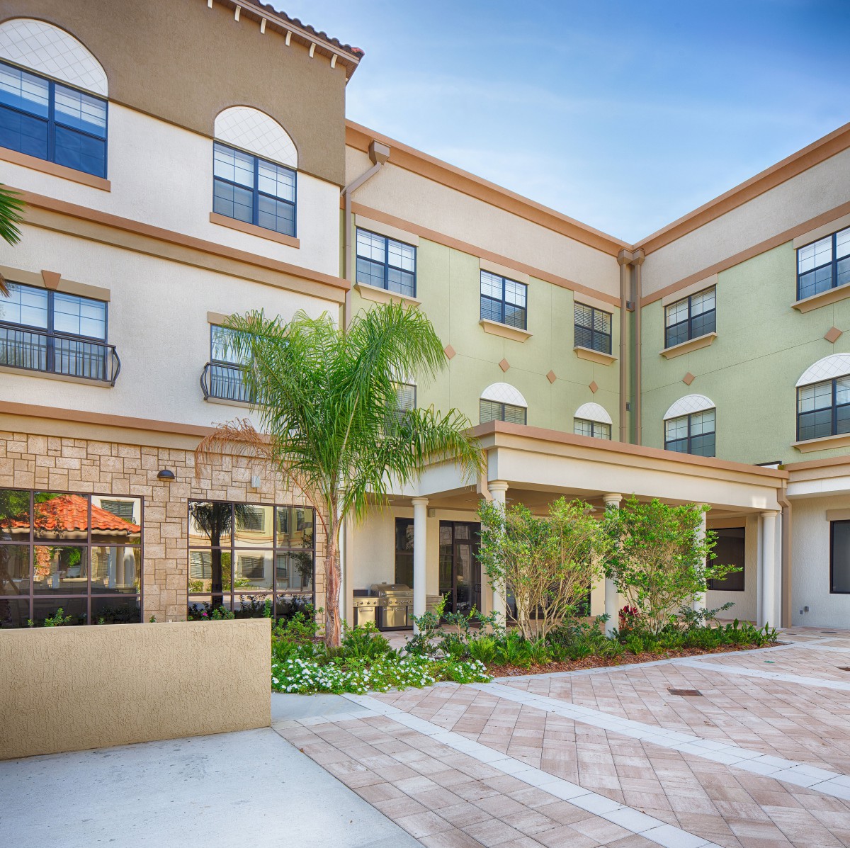 A modern residential building with a courtyard featuring palm trees and multiple windows.