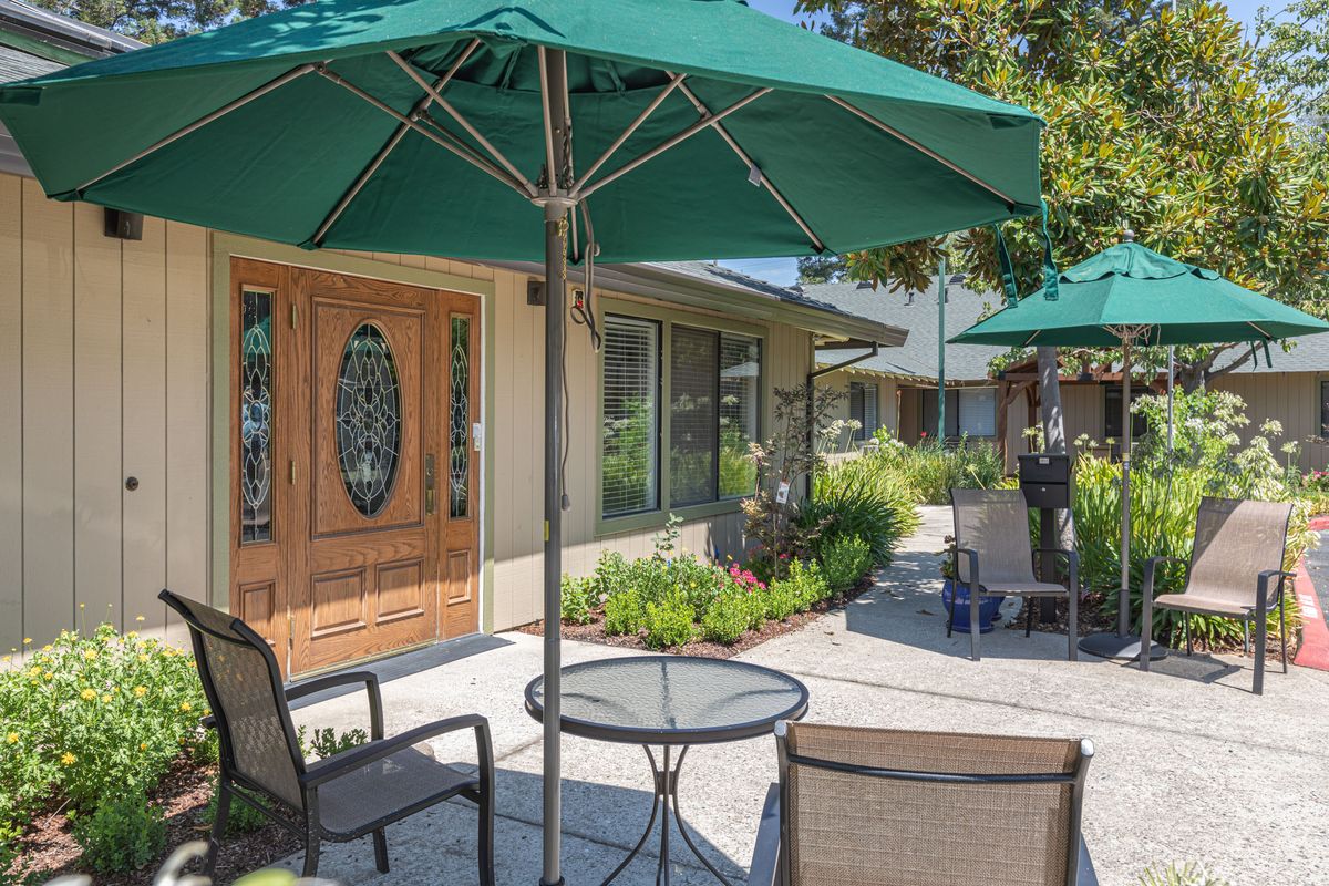 A sunny outdoor patio with a table, chairs, and large green umbrellas.