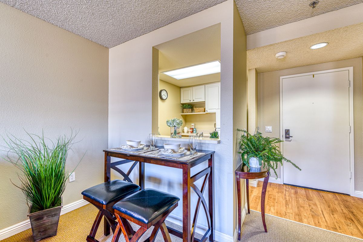 A cozy interior space featuring a small dining area with bar stools, adjacent to a kitchen, enhanced by decorative plants.
