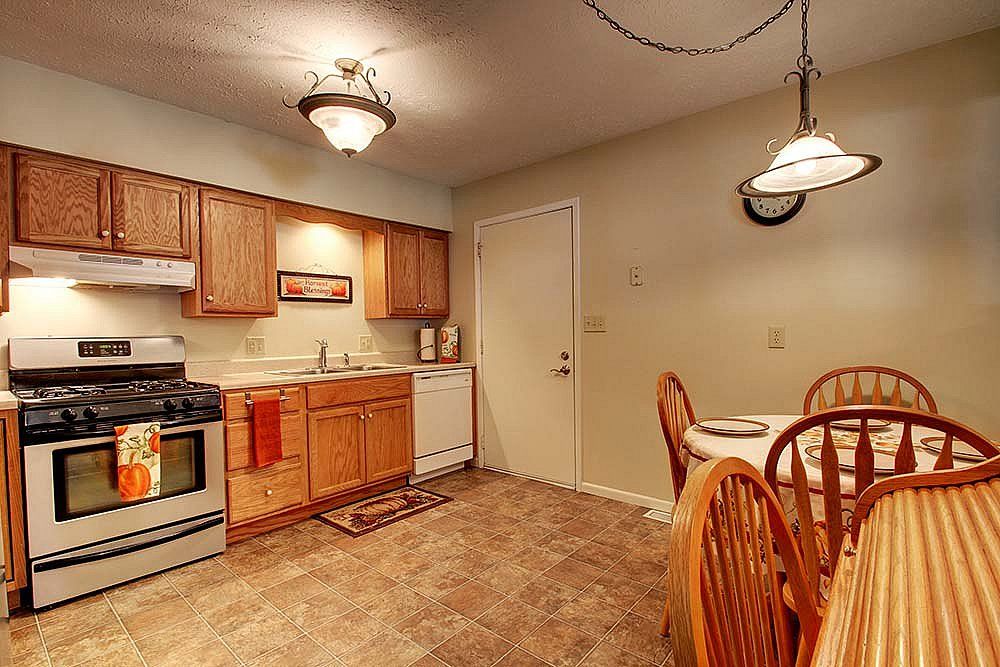 A cozy kitchen and dining area featuring wooden cabinets, a stove, a dishwasher, and a small dining table with chairs.