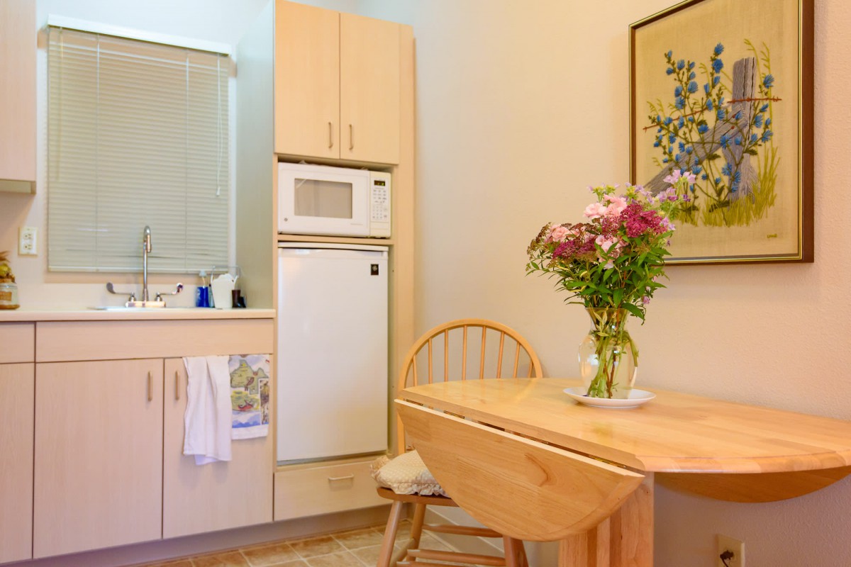 A cozy kitchen with a small dining area, featuring a wooden table with chairs and a vase of flowers.