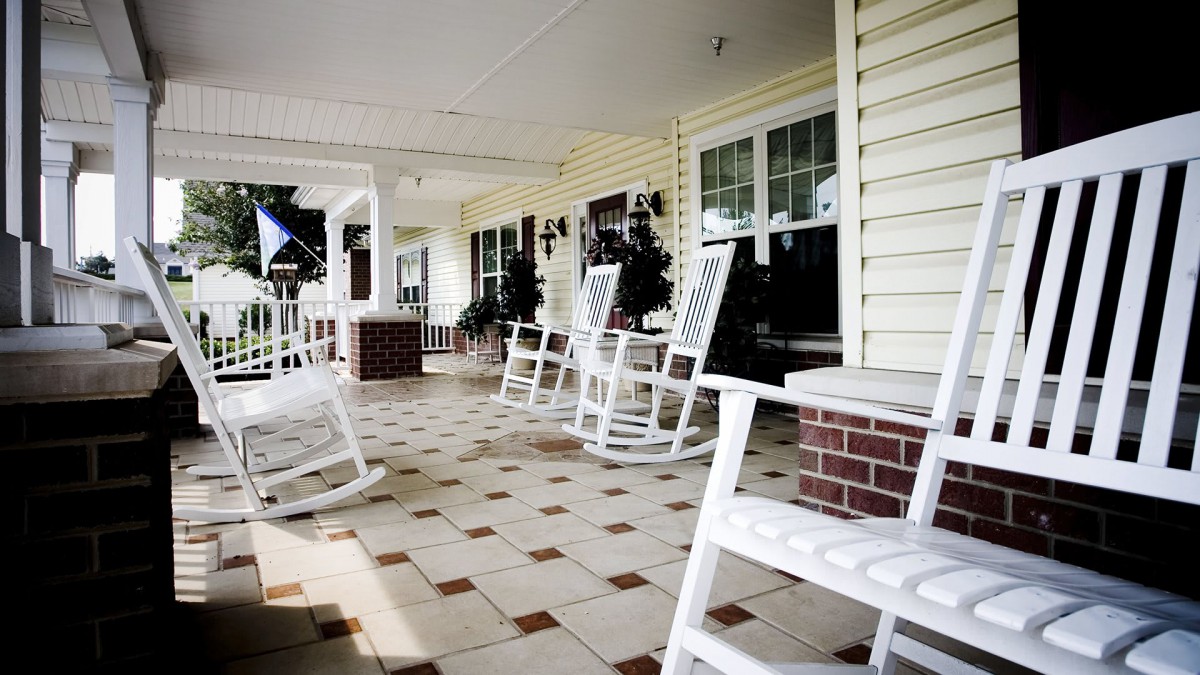 A cozy porch with white rocking chairs and a tiled floor.