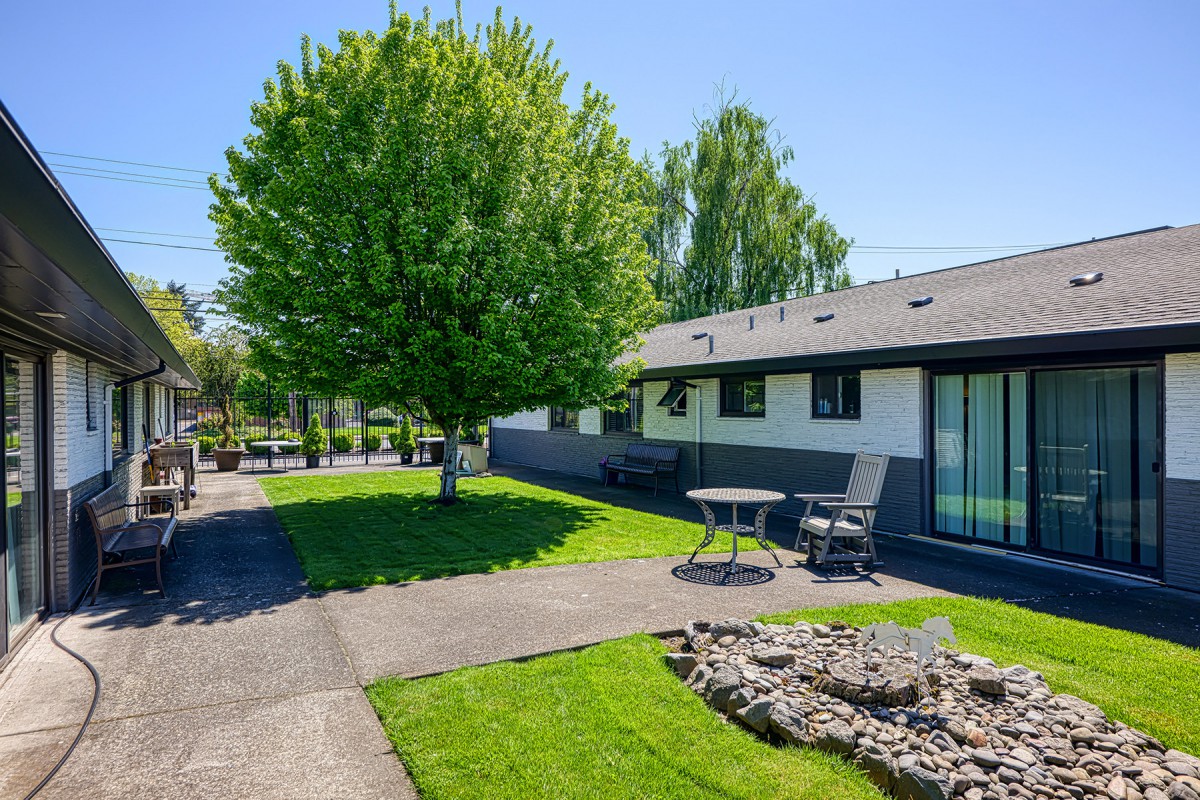 A well-maintained backyard with a lush green lawn, trees, and patio furniture next to a house.