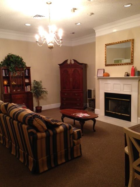 A cozy living room featuring a striped sofa, coffee table, and fireplace setup with a bookshelf and indoor plant in the corner.
