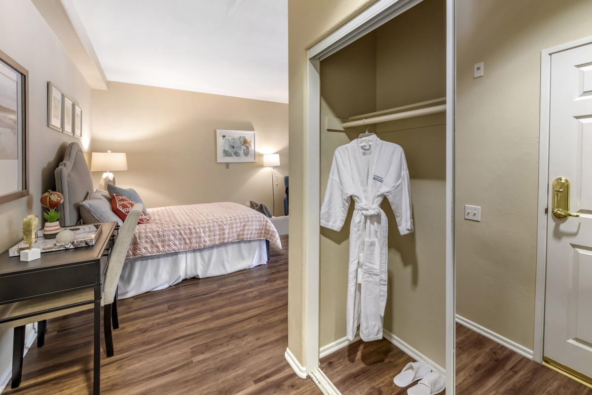 A cozy hotel room with a bed and a closet showcasing a plush robe.