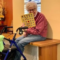 An elderly person holding a bingo card while sitting indoors with a walker.