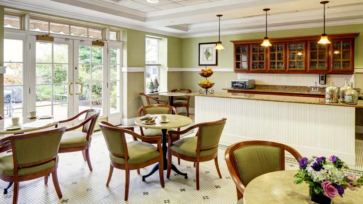 A cozy cafe interior featuring neatly arranged tables and chairs, a serving counter, and warm lighting.