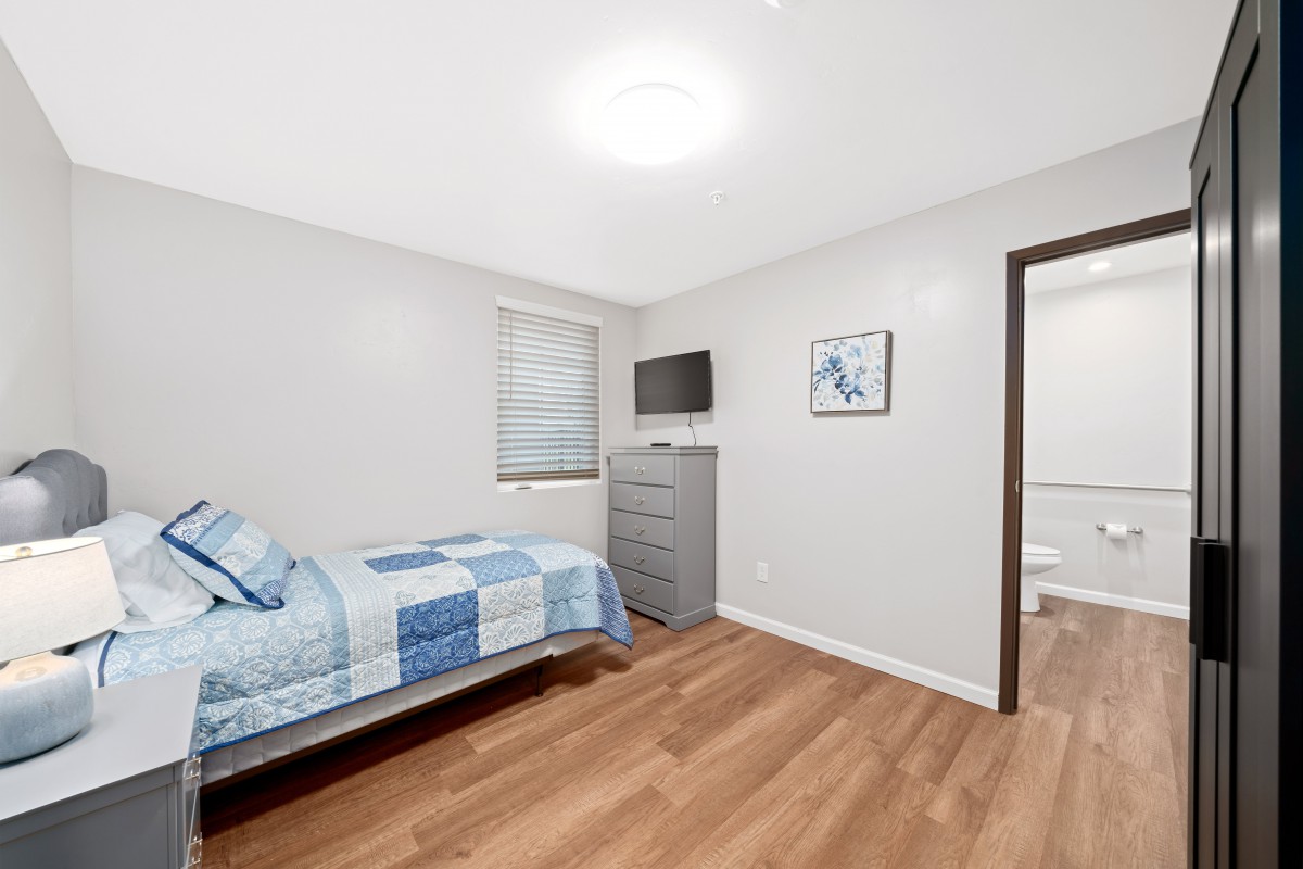A modern, minimalist bedroom with a single bed, wooden flooring, and wall-mounted TV.