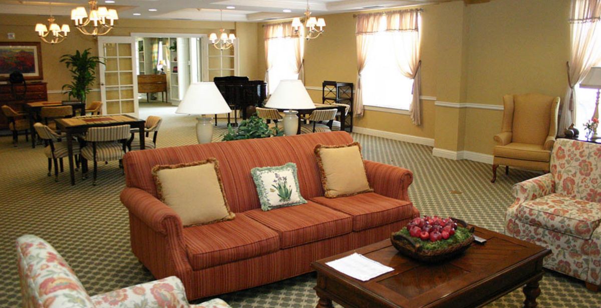 A cozy living room with a red sofa, decorative pillows, and a grand piano in the background.