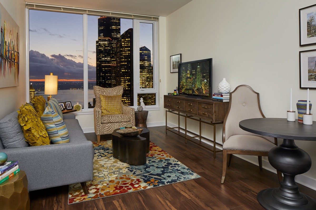 A modern living room with a cityscape view, featuring a cozy sofa, armchair, and vibrant rug.