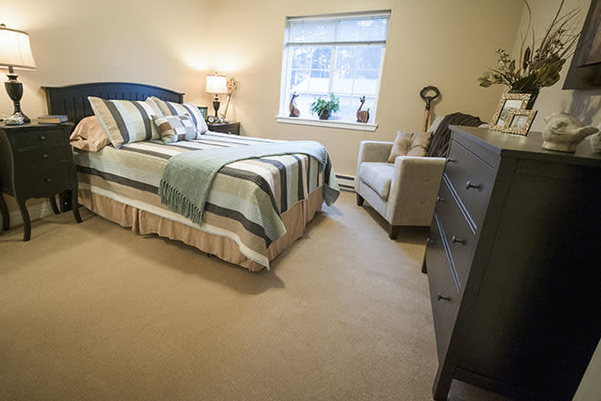 A cozy bedroom with a neatly made bed, a lamp on the bedside table, and a comfortable chair by the window.