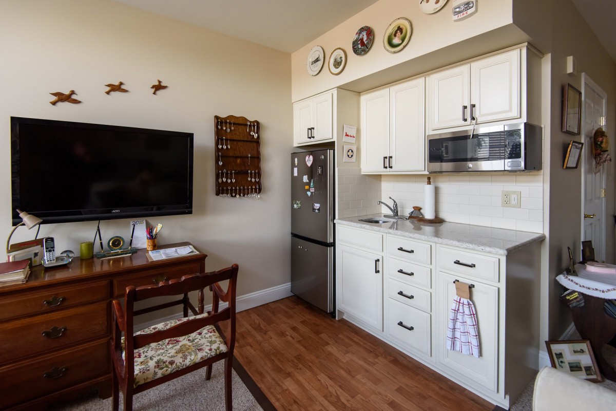 A cozy kitchen and dining area with white cabinets, a mounted television, and decorative plates on the wall.