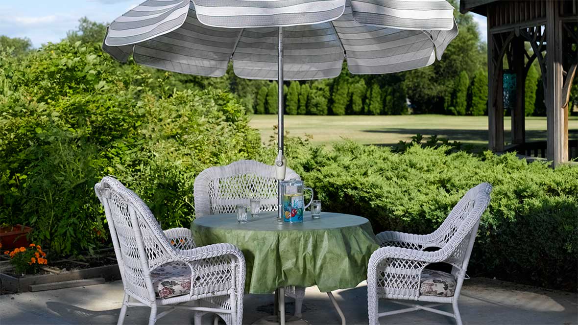 A cozy outdoor patio setup with a table, chairs, and an umbrella amidst lush greenery.