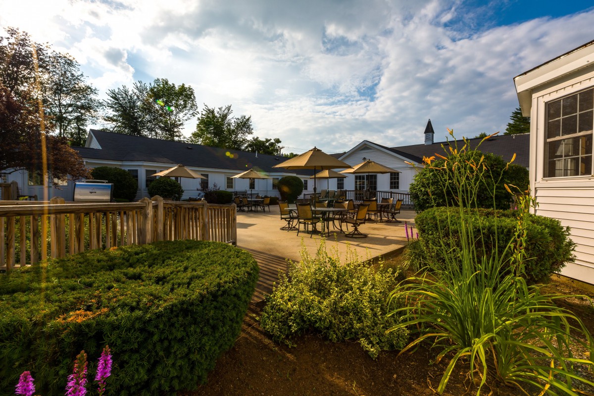 A tranquil garden with outdoor seating and a building in the background under a partly cloudy sky.