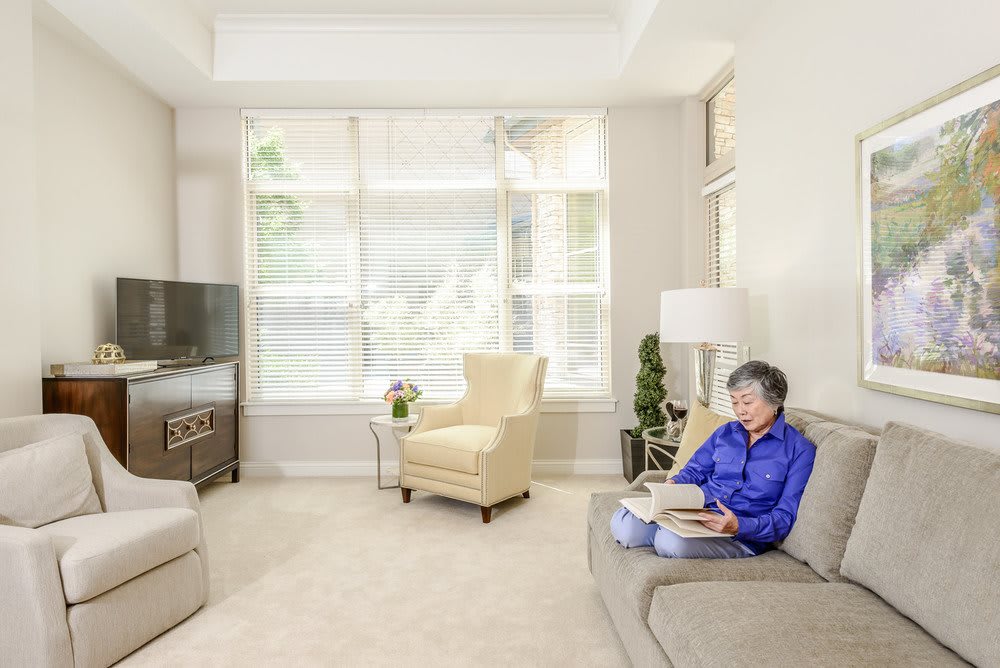 A senior woman reads a book in a cozy, well-lit modern living room.