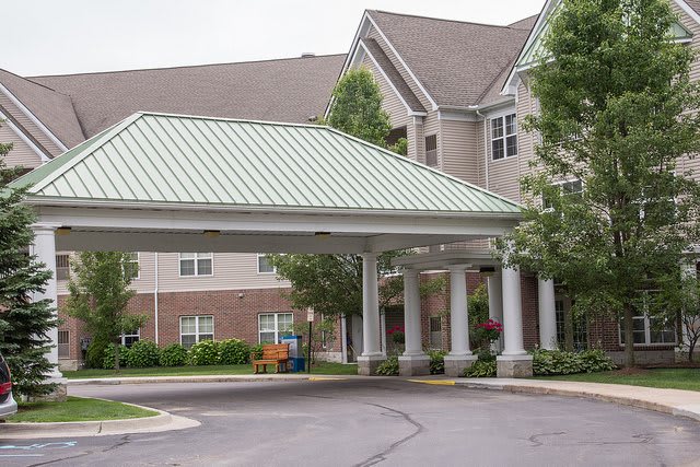 A building entrance with a covered canopy and columns surrounded by trees.