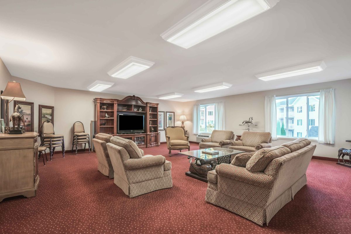A spacious living room with multiple couches, a television, bookshelves, and a central coffee table on a red carpet.