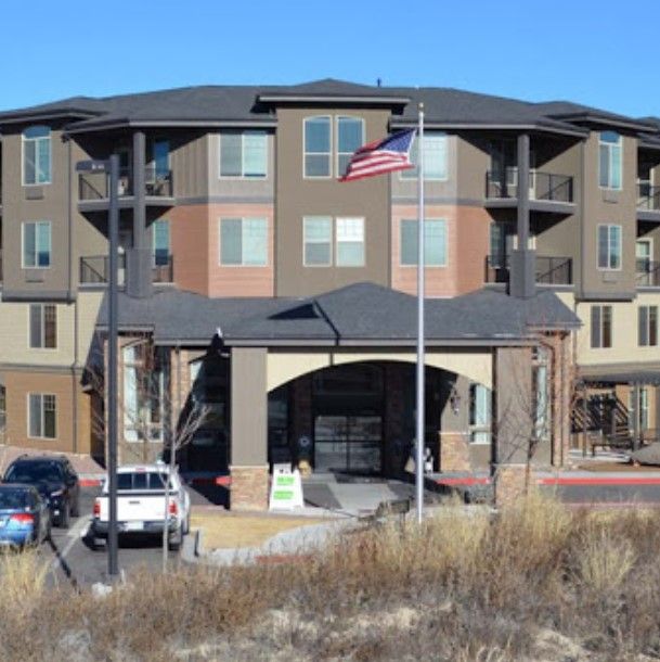 A modern apartment complex with an American flag in front and parked cars nearby.
