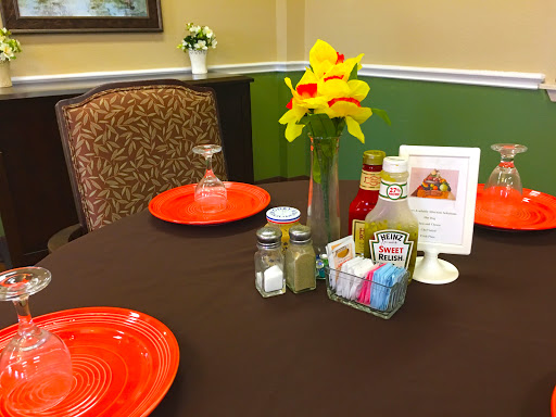 A cozy restaurant table set with orange plates, condiments, and a vase of vibrant flowers.