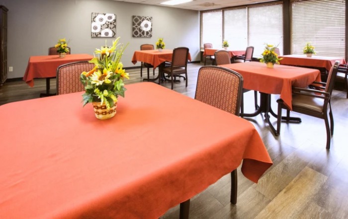 A dining room with tables covered in red tablecloths, decorated with flower arrangements.