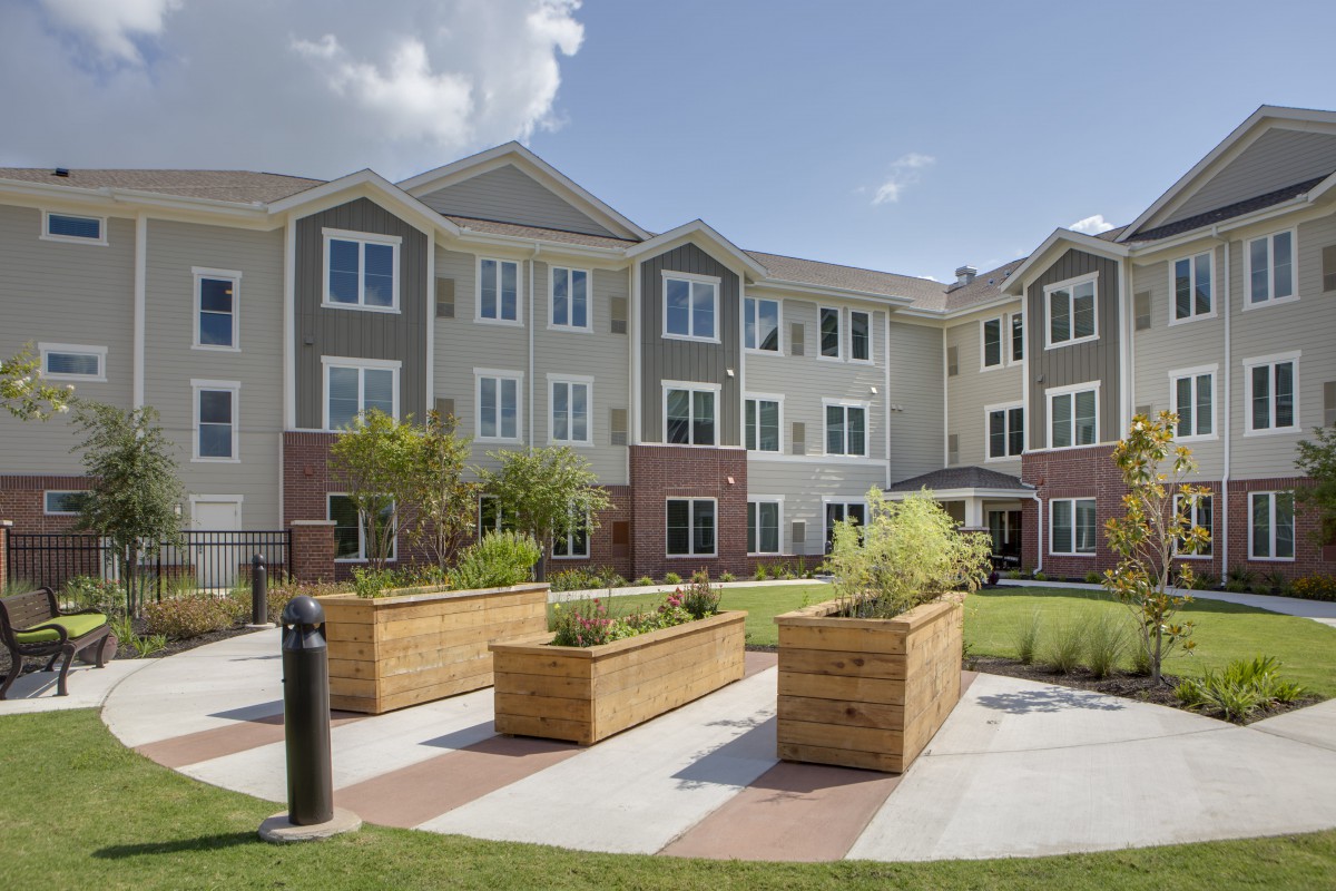 A modern apartment complex with landscaped garden areas and a clear sky.