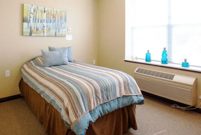 A cozy bedroom with a single bed featuring striped bedding, decorative pillows, and a bright window letting in natural light.