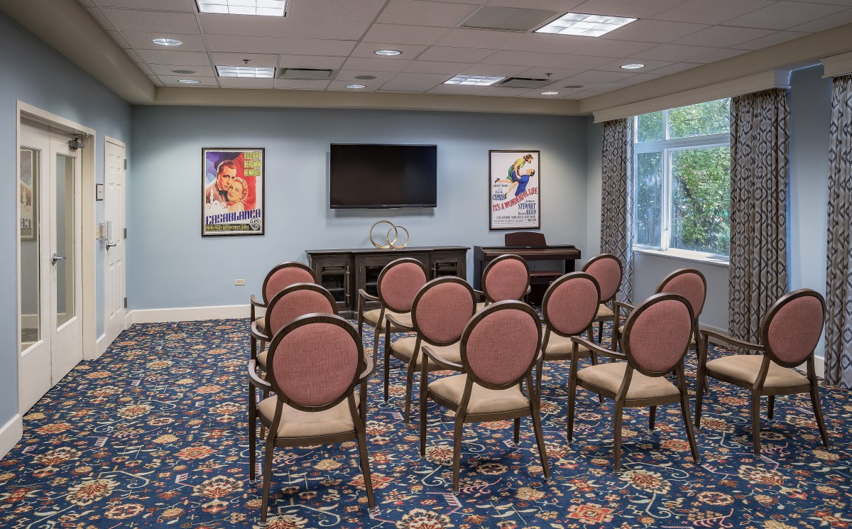 A small conference room set up with chairs facing a television screen, featuring decorative carpet and wall posters.