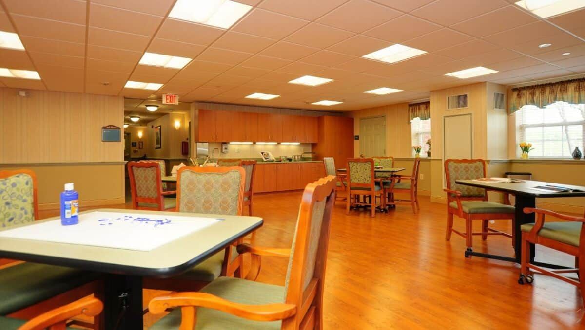 An empty dining area with wooden floors, tables, and chairs under bright lighting.