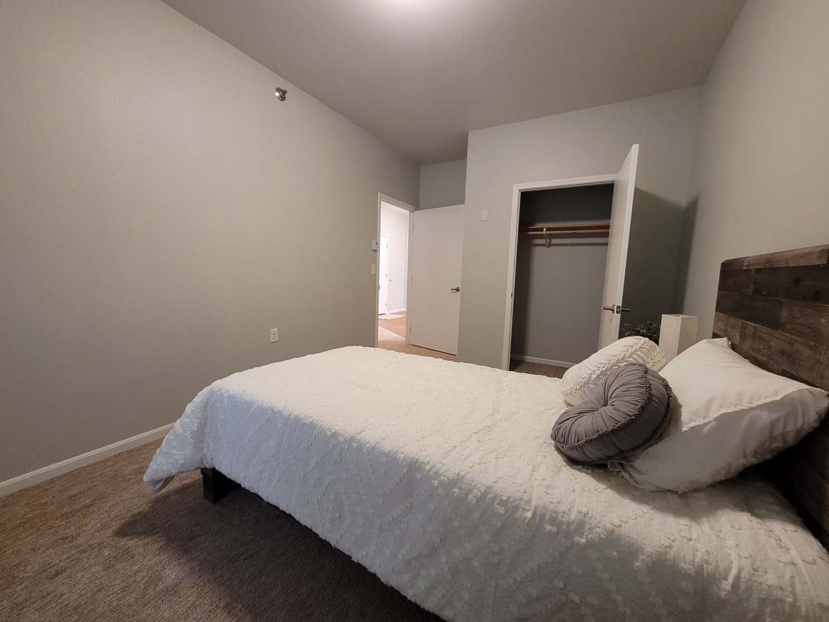 A minimalist bedroom with a neatly made bed and an open closet.