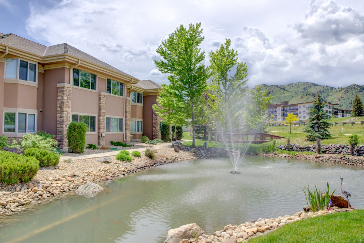 A scenic view of a building near a pond with a fountain and surrounding trees.
