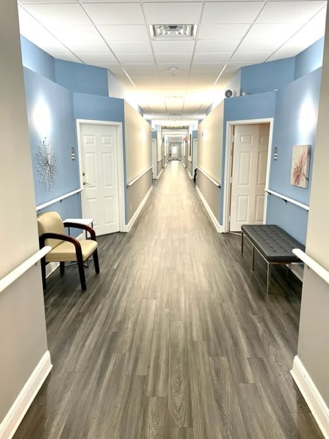 A brightly lit hallway with blue walls, featuring chairs and a bench along the sides.