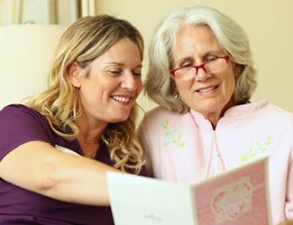 An elderly woman and a younger woman enjoying reading together.