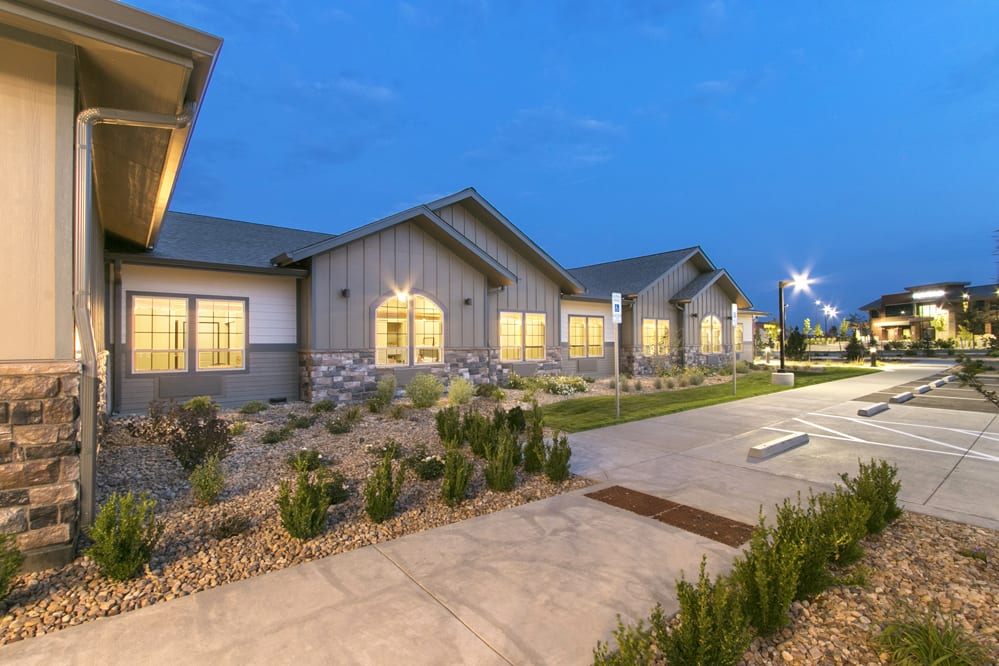 A modern building illuminated in the evening with a landscaped path and greenery.