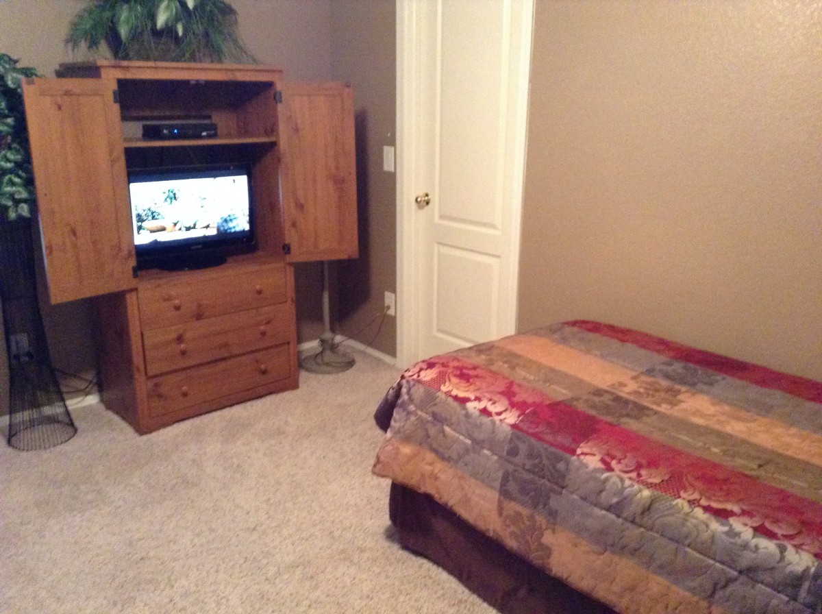 A cozy bedroom with a TV in a wooden cabinet and a colorful quilt on the bed.