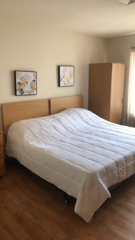 A cozy bedroom with a neatly made bed, two paintings on the wall, and wooden furniture.