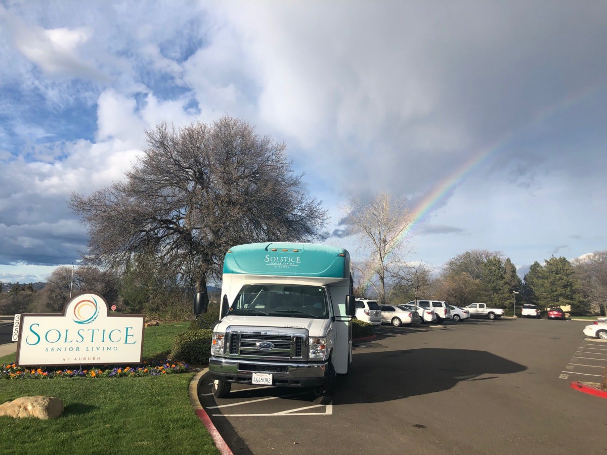 A truck parked beside a rainbow on a cloudy day.