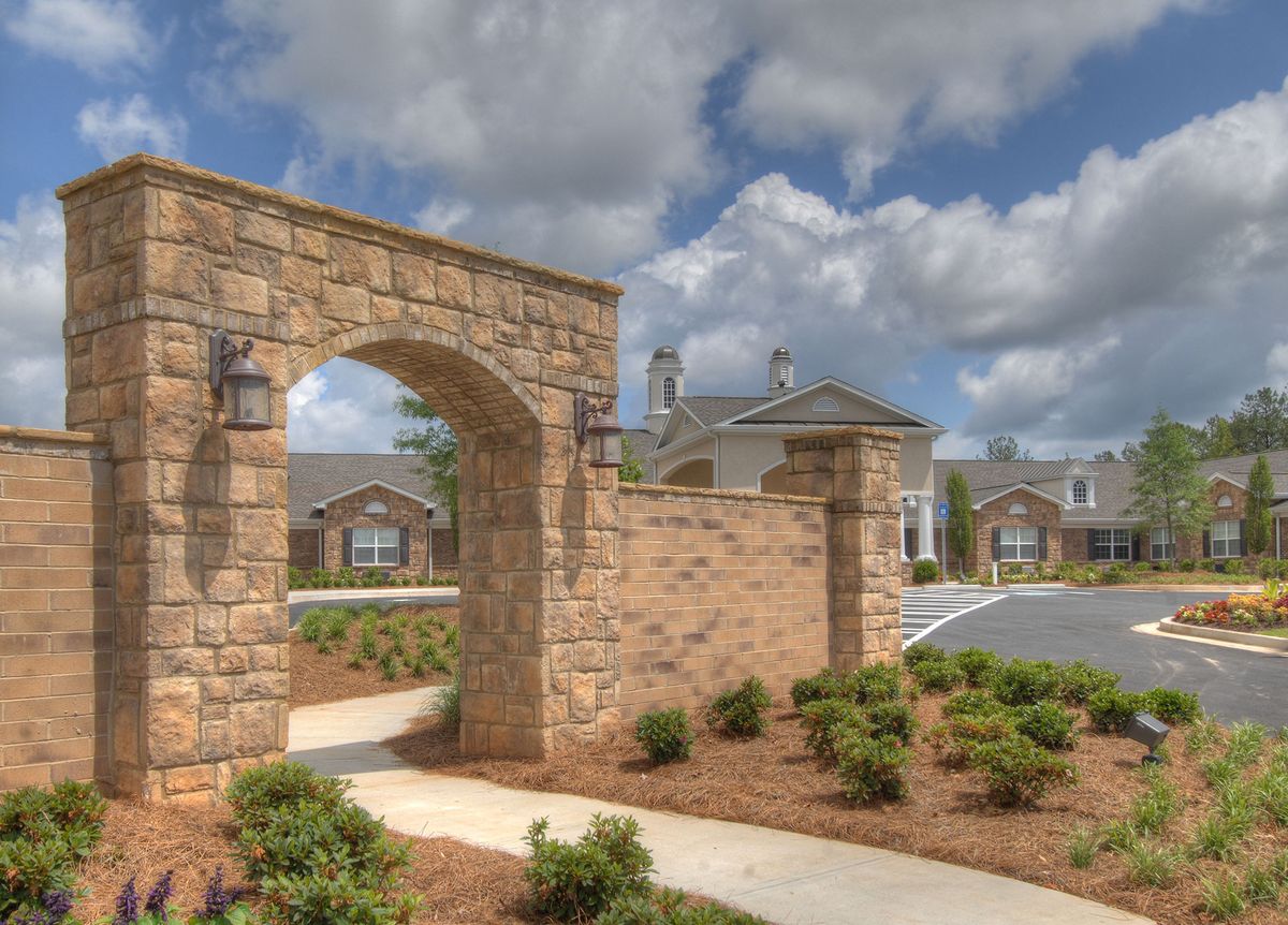 A picturesque stone archway leads to a residential community, surrounded by neatly maintained landscaping under a cloudy sky.