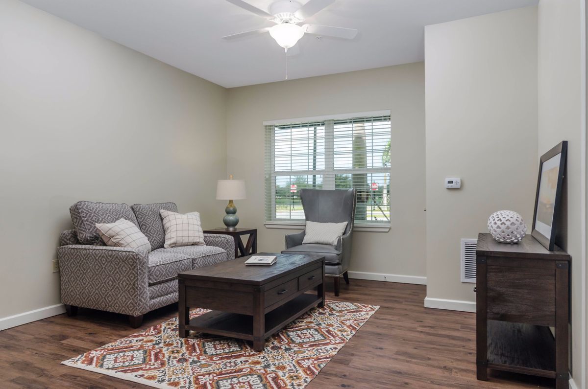 A cozy living room with a sofa, armchair, and coffee table, softly lit by a lamp next to a window.