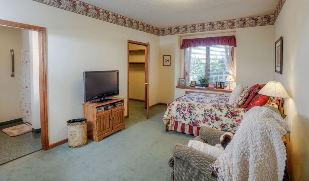 A cozy bedroom with floral bedding, a TV on a stand, and a window with scenic views.