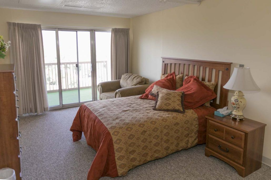 A cozy bedroom with a bed, armchair, and sliding glass doors leading to a balcony.